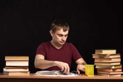 Man sits in front of an open book at the table and holds glasses with his hands. Stock Photos