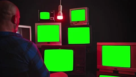 A man sits in front of a wall of televisions. Green screen. Chroma key. Video stock 168443283