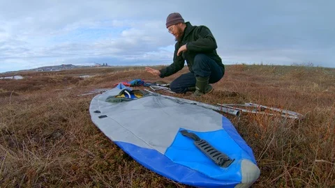 Man sits on grass and assembles light kayak to sail on river Stock Footage 123410874