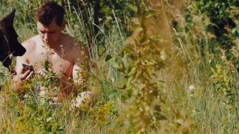 A man sits on the grass with German shepherd in the meadow and looking at the Stock Footage 111658582