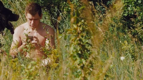 A man sits on the grass with German shepherd in the meadow and looking at the Stock Footage 111658611