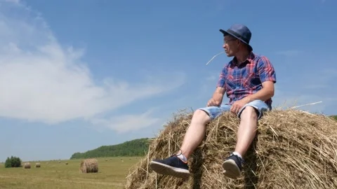A man sits on a haystack and then lies down. Stock Footage 135496675