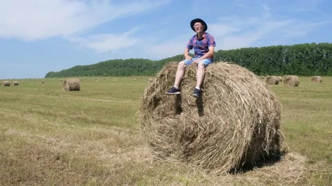 A man sits on a haystack and then lies down. Stock Footage 135496677