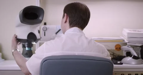 The man sits with his back and looks into the microscope. Dental laboratory Stock Footage 163906641