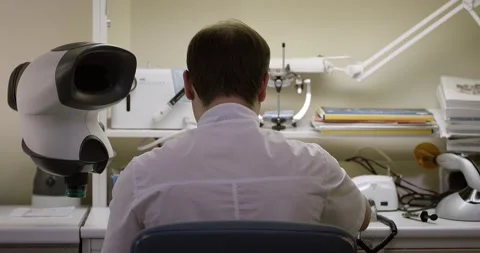 The man sits with his back and looks into the microscope. Dental laboratory Stock Footage 163908325