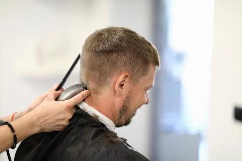 Man sits with his back master hairdresser cuts his hair with machine Stock Photos