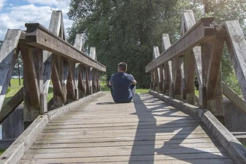 The man sits with his back turned on an old wooden bridge Stock-Fotos