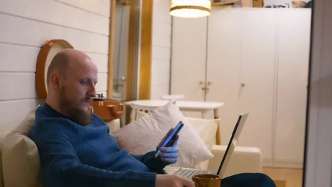 A man sits at home on the couch in the evening, drinks his coffee and works on a Stock Footage 171671167
