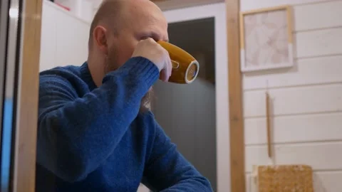 A man sits at home in the evening at the table drinking coffee in front of a Stock Footage 171198621