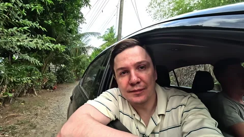 Man sits inside car looking out open window at tropical roadside Stock Footage 307487402