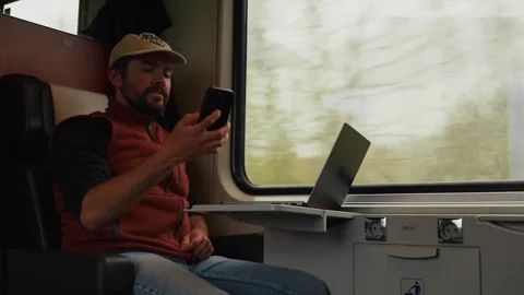 A Man Sits Inside a Train, Looking Out the Window While Working on His Laptop Stock Footage 333795746