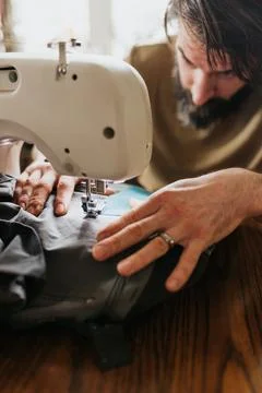 Man sits at kitchen table with sewing machine patching work pants Stock Photos