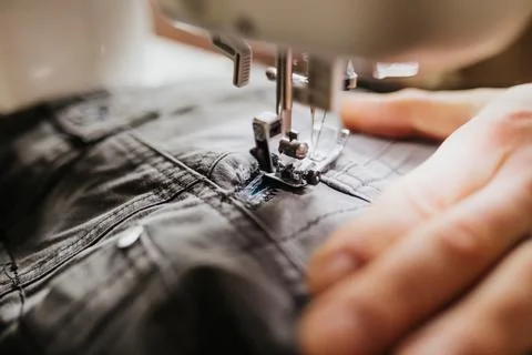 Man sits at kitchen table with sewing machine patching work pants Stockfoto's