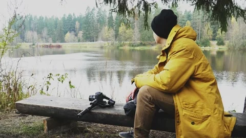 A man sits by the lake on a bench. next to a tree. Stock Footage 142491498