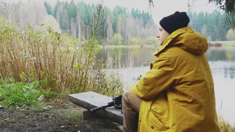 A man sits by the lake on a bench. next to a tree. Stock Footage 166095687