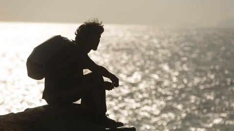 A man sits on a large stone. on the background of the ocean. silhouette of a man Video stock 128437384