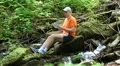 Man sits near small river in the forest and communicates via tablet computer HD Footage