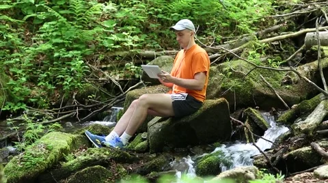 Man sits near small river in the forest and communicates via tablet computer 스톡 동영상 59143137