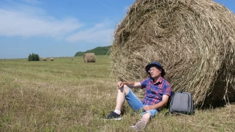 A man sits next to a haystack and enjoys nature. Stock Footage 135458082