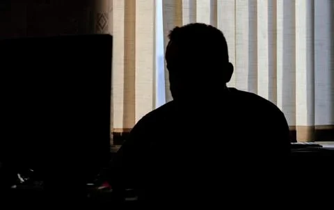 Man sits in the office at the computer. only silhouette. he looks at the came Foto stock