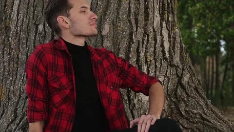 A man sits outside by a tree Stock Footage 168840671
