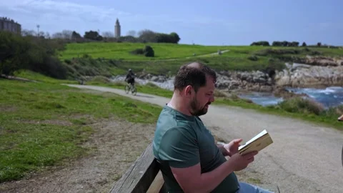 A man sits on a park bench reading a book. Stock Footage 189915851