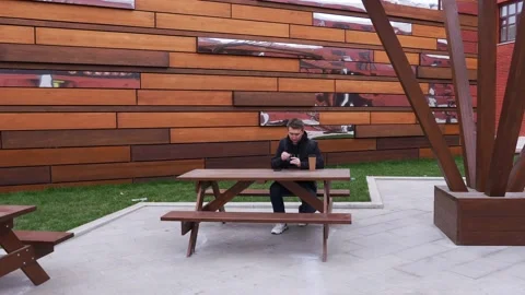 A man sits in a park, puts on wireless headphones in his ears, listens to music Stock Footage 141786985