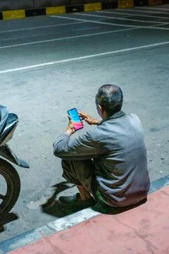 Man sits on pavement, using smartphone Stock Photos