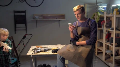 Man sits with phone, boy plays with wood gun, slow motion Stock Footage 126716937