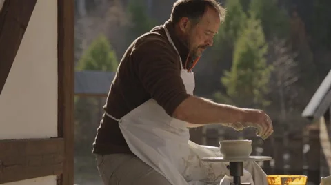 Man sits at pottery wheel in open air and creates jar in nice sunny day Video stock 64646496