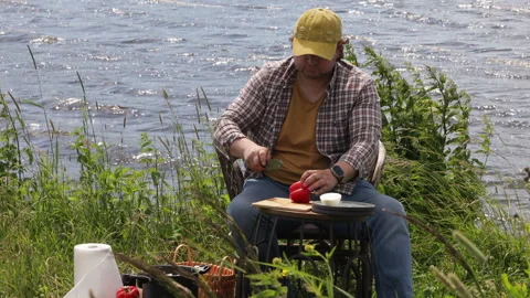 A man sits on a river bank on a summer day against the background of water and p Video stock 278535711