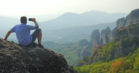 Man sits on rock and makes selfies and panorama of Meteora valley Video stock 298943672