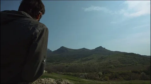 A man sits on a rock in the background of a mountain ridge Stock Footage 75672465