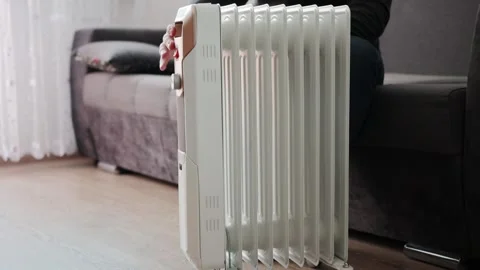 A man sits on a sofa and moves an electric heater on wheels across the floor Stock Footage 254060296
