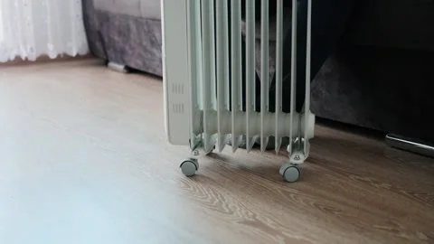 A man sits on a sofa and moves an electric heater on wheels across the floor Stock Footage 255634502