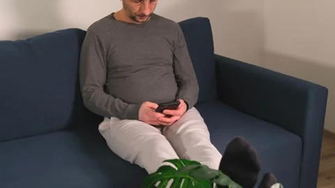 A man sits on a sofa and scrolls through his phone. Stock-Footage 322093019