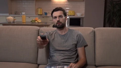 Man sits on sofa and uses remote control. He starts to eatch TV. Then suddenly Stock-Footage 99739267