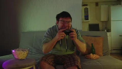 A man sits on a sofa, plays a video game on gamepad and exults in victory 库存影片 314395947