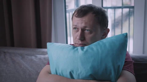 Man sits on the sofa, presses a cushion to himself and thinks, feels morally bad Stock Footage 309211615
