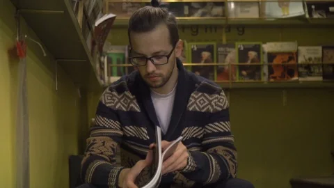 A man sits on the steps and leafs through the magazine. Book store or library 動画素材 101721225