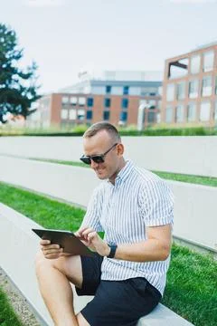 Man sits on steps using tablet in urban area with buildings in background d.. Stock Photos