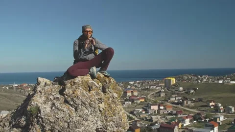 A man sits on a stone against the background of the sea and the valley with the Stock Footage 131709351