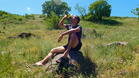 A man sits on a stone and drinks water 스톡 동영상 196802678