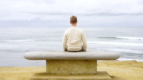 Man sits on a stone bench and looks out at ocean on the shore of San Diego Stock Footage 154805289