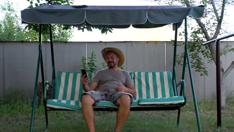 A man sits on a swing and communicates via video link 4K Stock Footage 160110182
