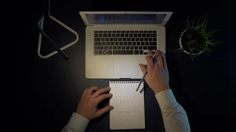 A man sits at a table and draws a graph of income in a notebook while sitting at Stock Footage 102331353