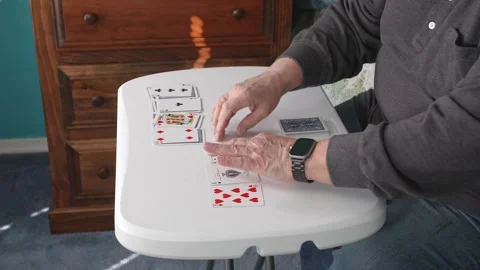 A man sits at a table and plays with solitaire cards. He arranges them and Vidéo 336109090