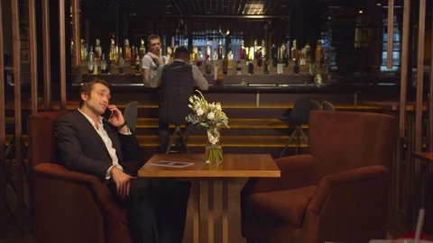 Man sits at a table in a cafe and talks on the phone Stock Footage 123695985