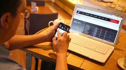 Man sits at table in cafe with phone and laptop which launched a website Stock Footage 73728364
