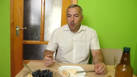 A man sits at the table eating fresh fruit with a fork, enjoying a light home Stock Footage 337883665